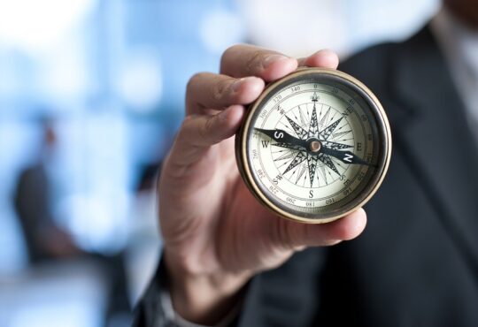 Business man holding a compass with a corporate background
